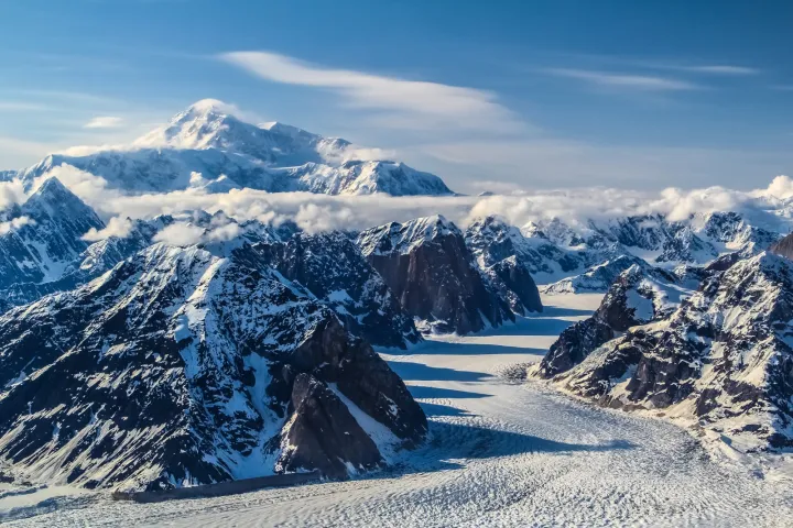 Aerial view of snow-covered mountains and glaciers under a clear blue sky.
