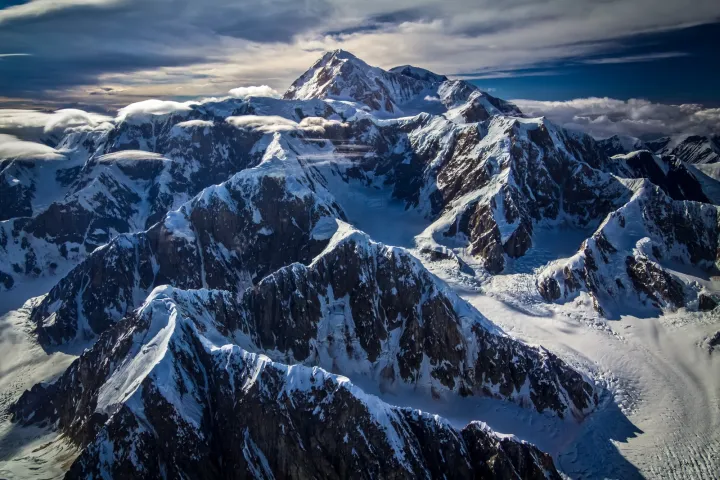 Snow-covered mountain range with dramatic clouds and shadows.