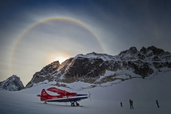 Red plane on snowy ground with mountains and a halo around the sun.